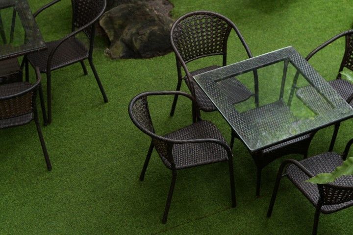 A high-angle view of outdoor wicker-style chairs surrounding a square glass-topped table on a green artificial lawn.