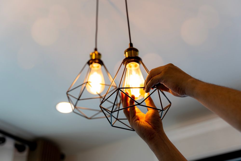 Hands Replacing a Lightbulb in a Geometric Pendant Lamp — Rohr Electrical in Wellington, NSW