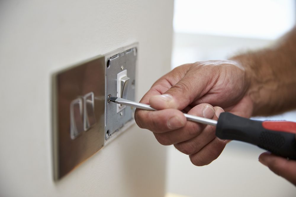 Person Uses a Screwdriver to Work on a Light Switch on a Wall — Rohr Electrical in Wellington, NSW