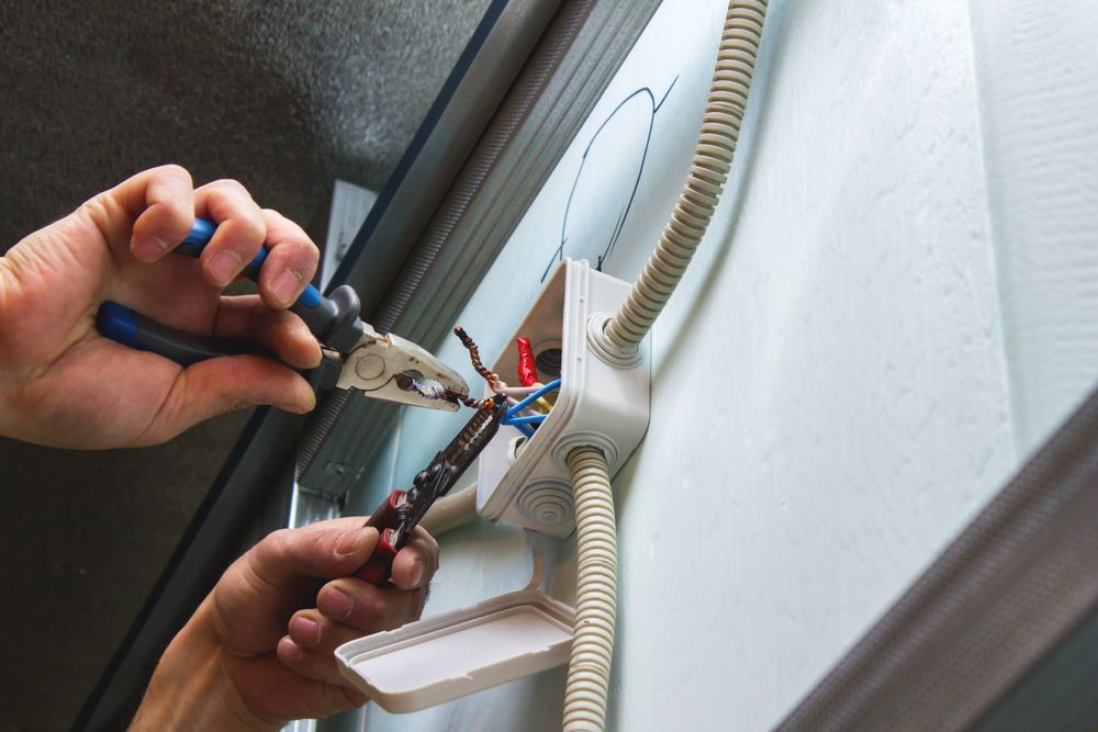Electrician's Hands Using Pliers to Cut Wires in an Electrical Box on a Wall — Rohr Electrical in Gilgandra, NSW