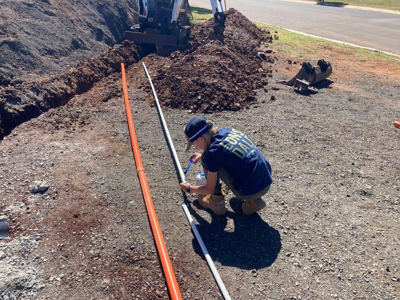 Man Kneels Beside Trench, Measuring White Pipe — Rohr Electrical in Dubbo, NSW