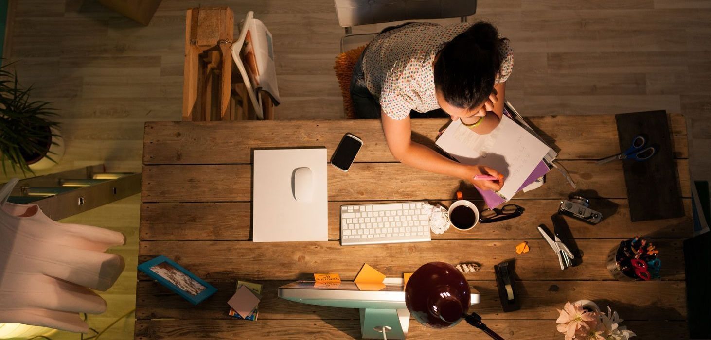A woman is sitting at a wooden desk working on a computer.