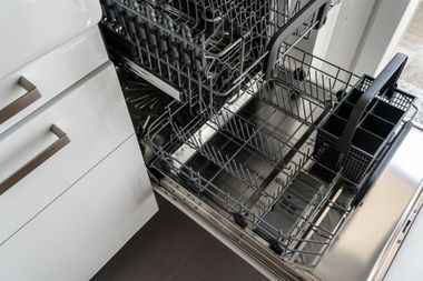 Kitchen dishwasher racks pulled out, showing empty metal baskets beside white cabinets and a countertop
