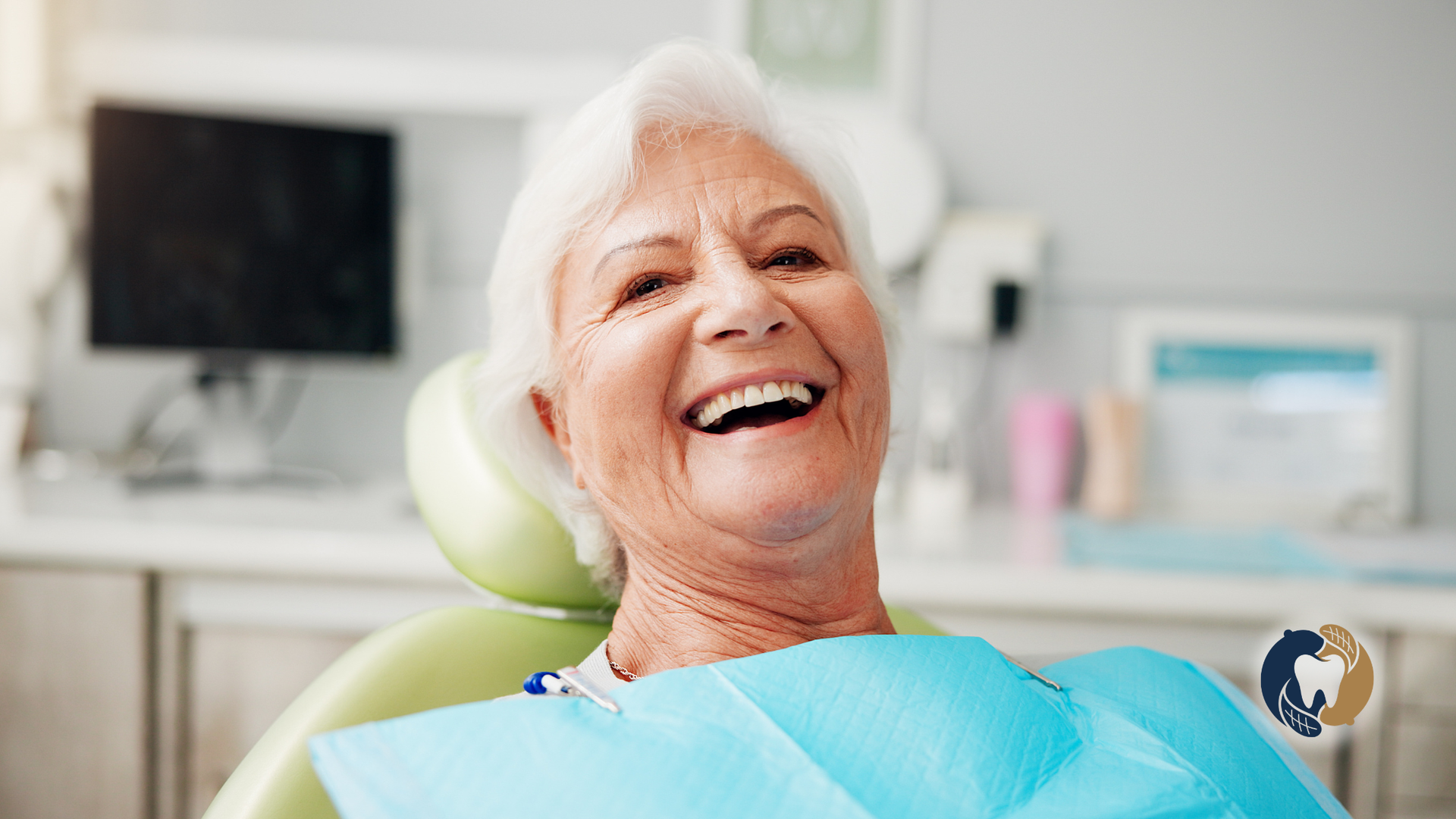 Smiling patient reclining in a dental chair with a blue bib in a bright clinic