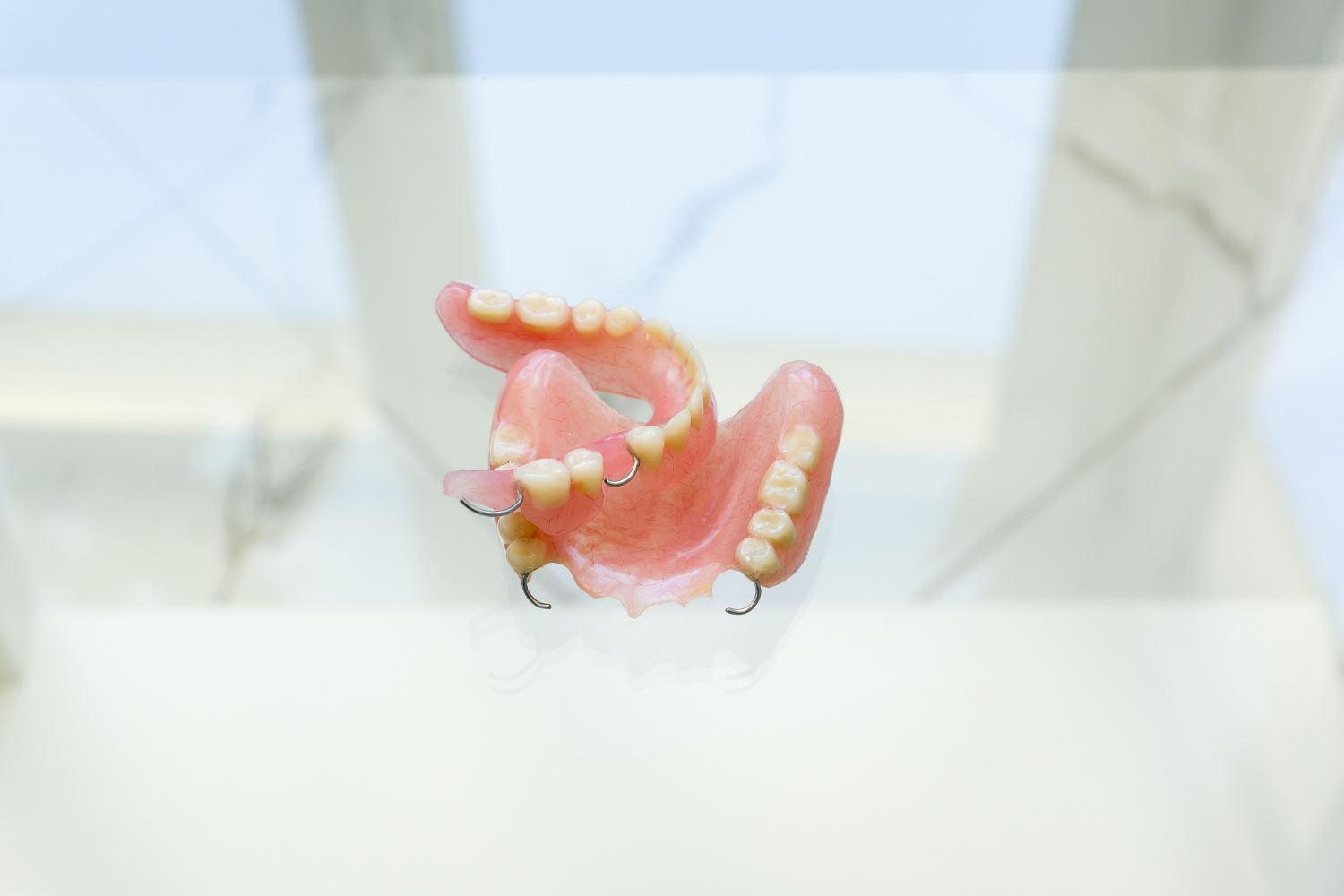 A partial dental prosthesis with pink acrylic base and metal clasps, resting on a white surface.