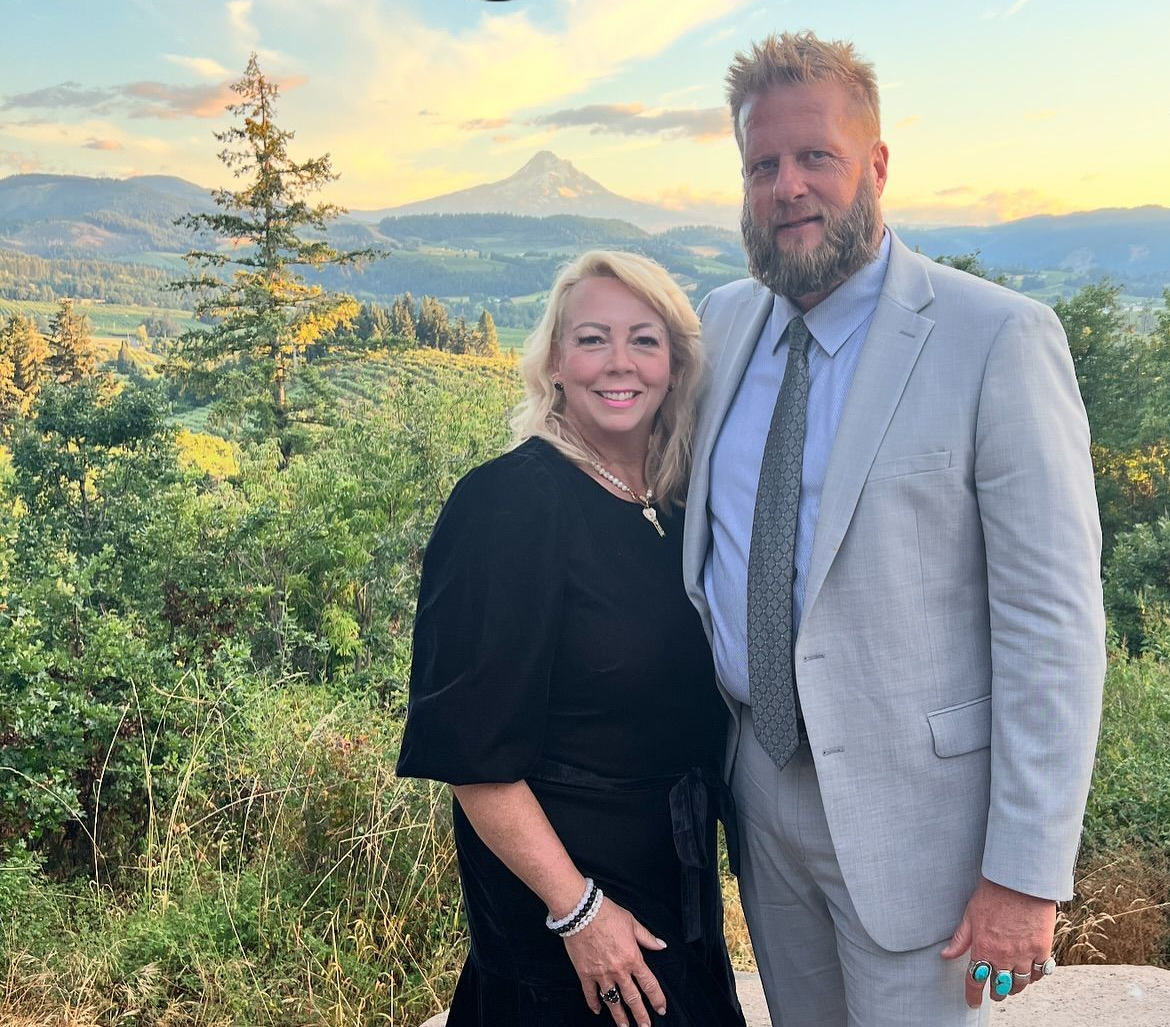 Couple posing outdoors with mountain and sunset in background.