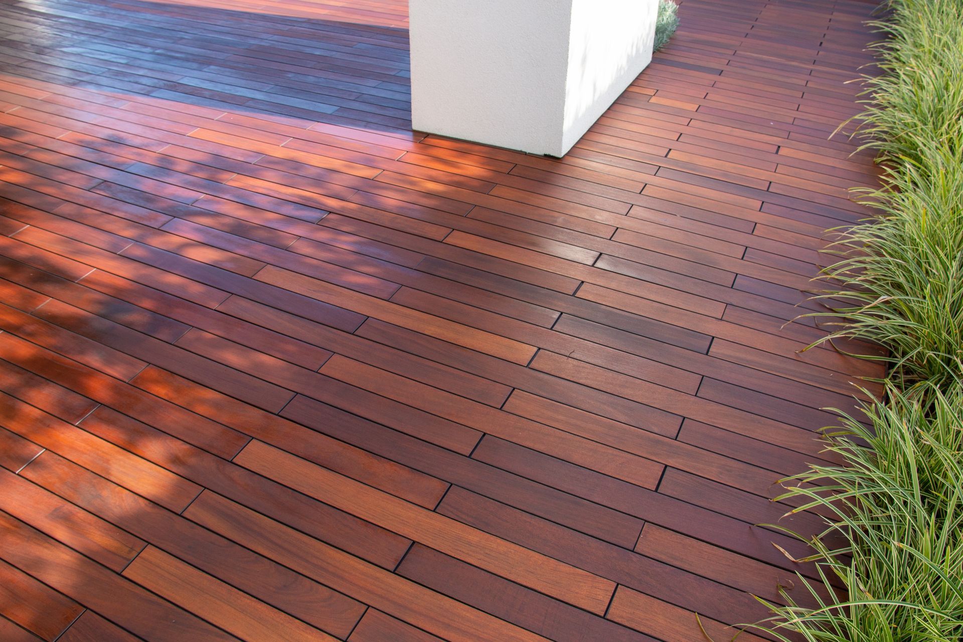 Wooden deck with reddish-brown planks beside a white column and green ornamental grass