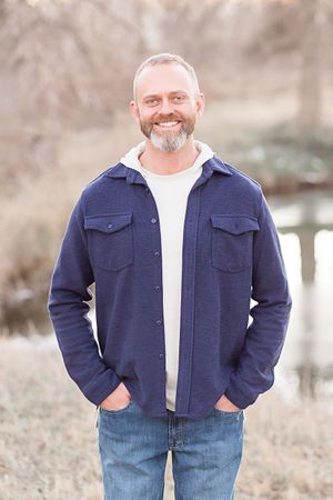 A man wearing a blue jacket and jeans is standing in a field with his hands in his pockets.