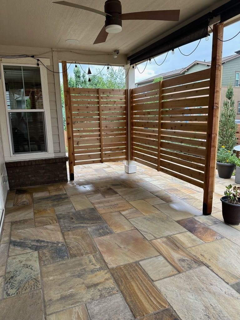 A patio with a wooden fence and a ceiling fan.