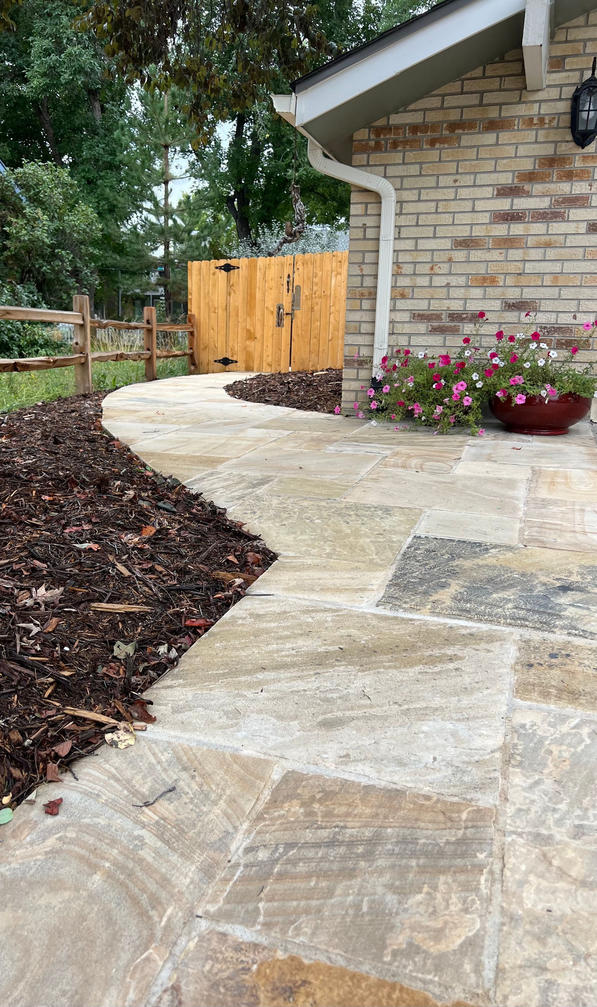 A stone walkway leading to a brick house with a wooden fence.