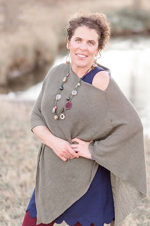 A woman wearing a poncho and a necklace is standing in a field.