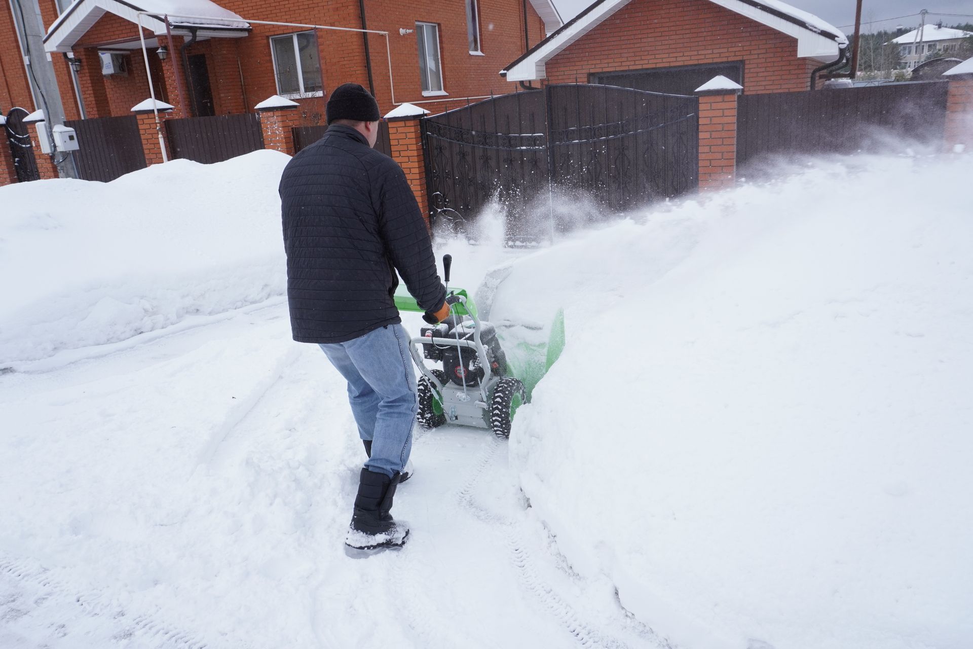 A man is using a snow blower to clear a snowy driveway.
