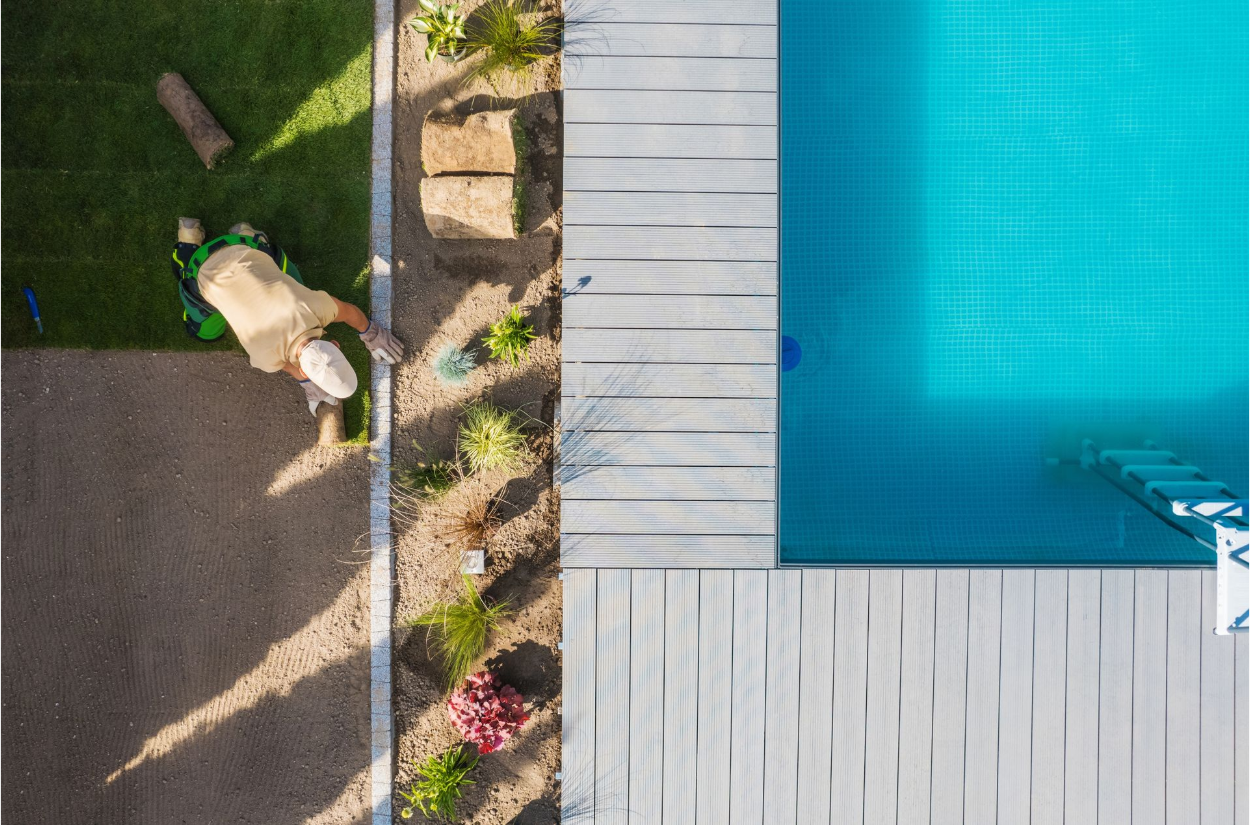 An aerial view of a man cutting grass next to a swimming pool.
