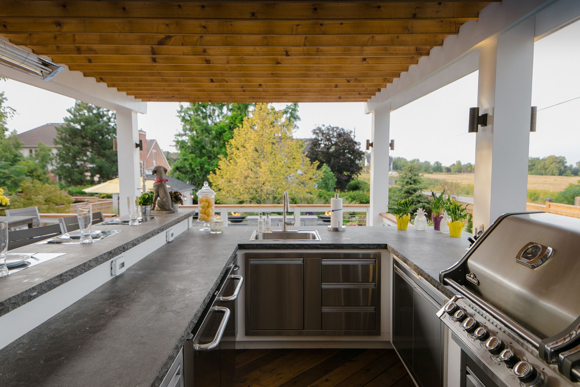 A kitchen with a grill and a sink under a pergola.