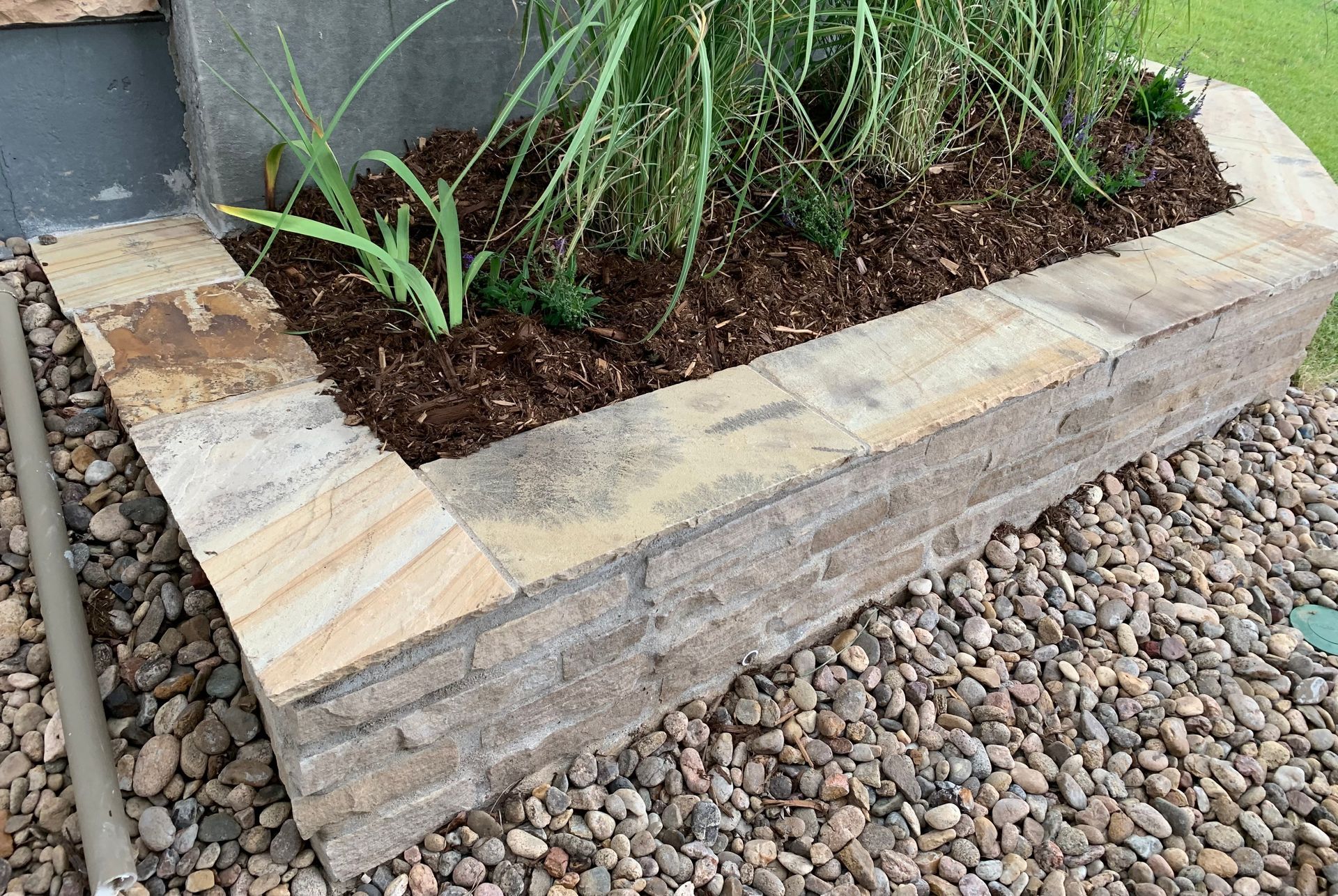 A stone planter filled with plants is sitting on top of a pile of gravel.