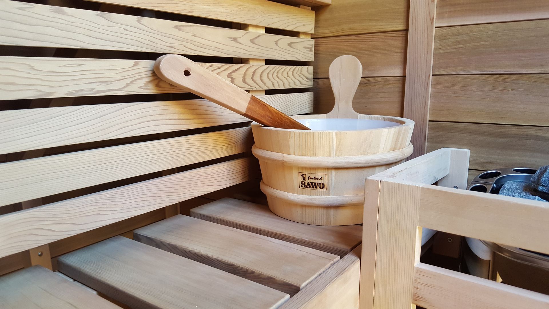 Wooden sauna interior with bench, ladle, and bucket beside a stove