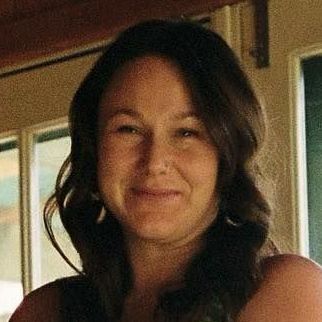 Smiling person with dark hair indoors near a window and wood-paneled wall