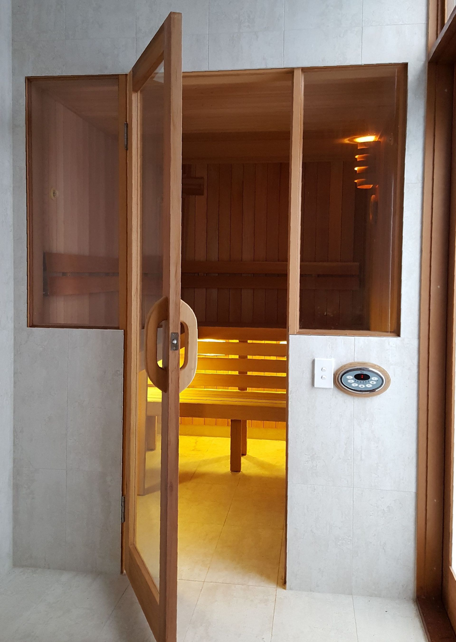 Open wooden sauna with warm yellow lighting and a glass door in a concrete hallway