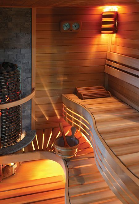 Wood-paneled sauna with curved wooden benches and a central heater glowing warm orange light.