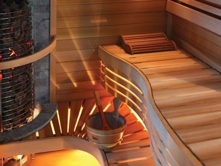 Modern sauna interior with wooden benches, curved seating, and a central stove with warm glowing coals