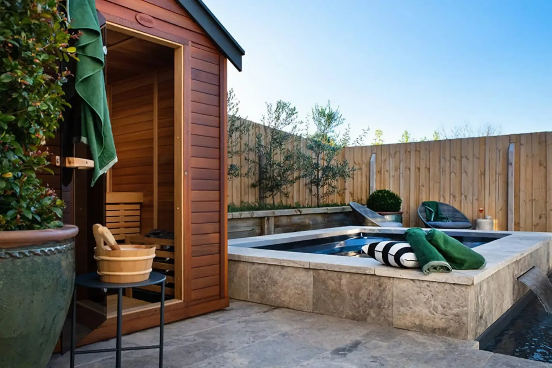 Backyard hot tub beside a wooden sauna, with towels and a fenced patio area