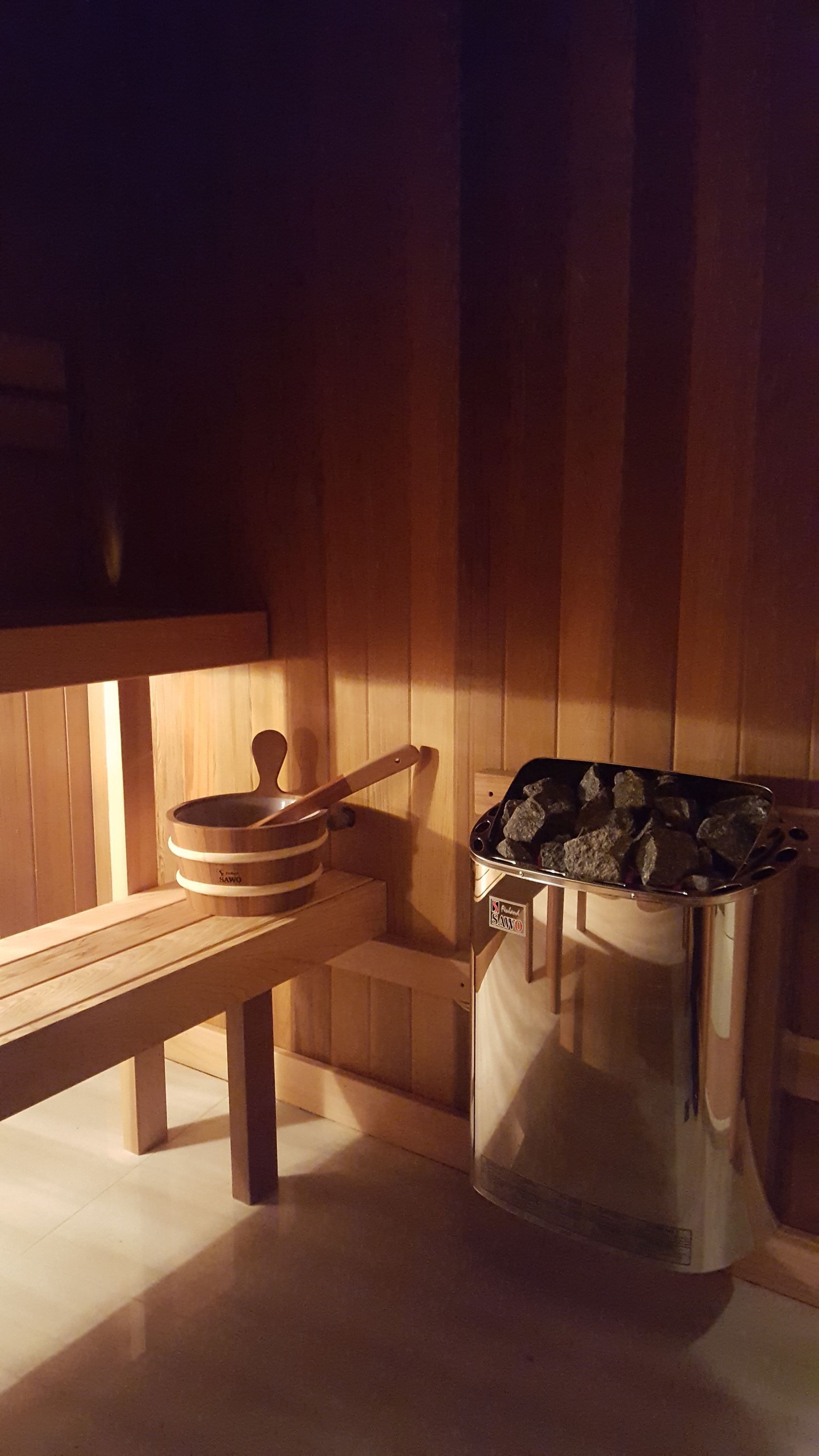 Wood-paneled sauna interior with a wooden bench, bucket, ladle, and towel rack.