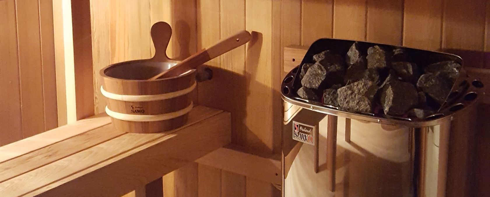 Wooden sauna bench with a ladle and a bucket of hot rocks in warm orange light