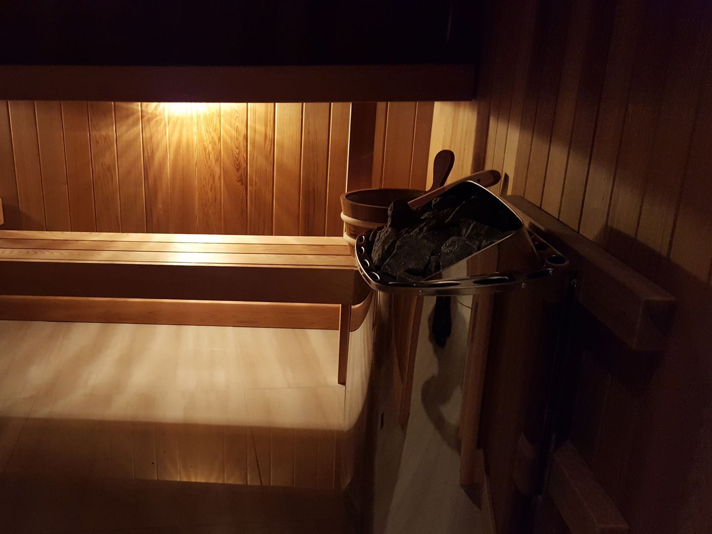 Wood-paneled sauna with wooden benches and a metal bucket on the right.