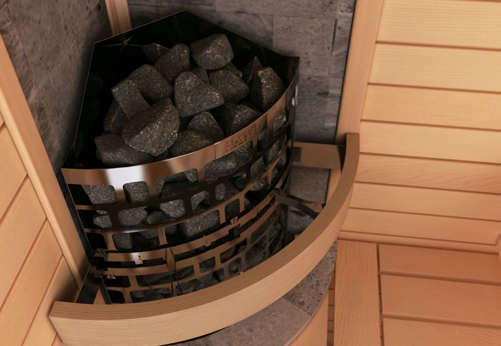 Circular sauna heater filled with dark rocks beside light wood paneling