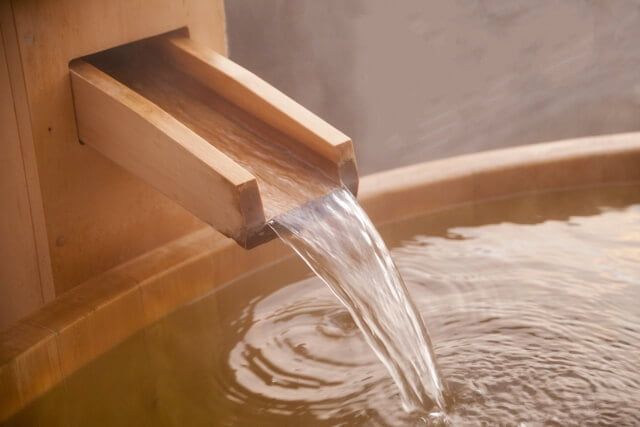 Water pouring from a wooden spout into a steaming bath