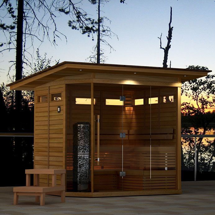 Wooden outdoor sauna with bench and frosted glass panels at sunset.