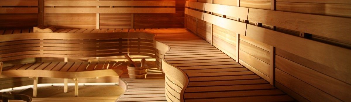 Wood-paneled sauna with wooden benches, warm amber lighting, and stacked towels.