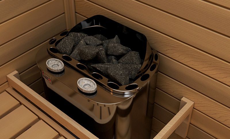 Stainless steel sauna heater filled with black stones in a wooden sauna corner