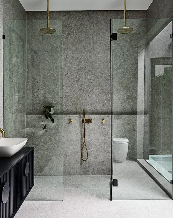 Modern gray bathroom with glass shower, double brass fixtures, and dark vanity