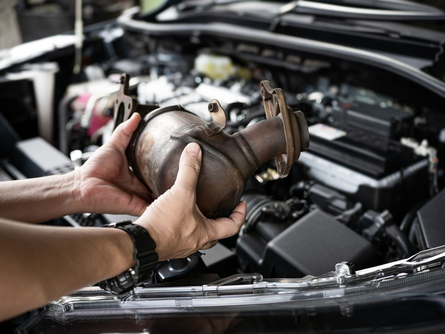 A person is holding a exhaust pipe in their hands in front of a car engine.