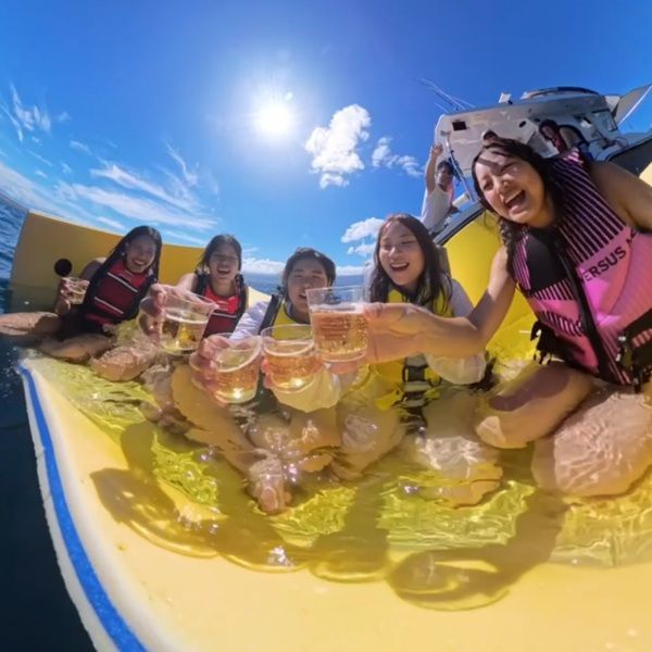 四個穿著救生衣的人放鬆地躺在漂浮在平靜開闊的海洋上的一張巨大的波浪形黃色墊子上。