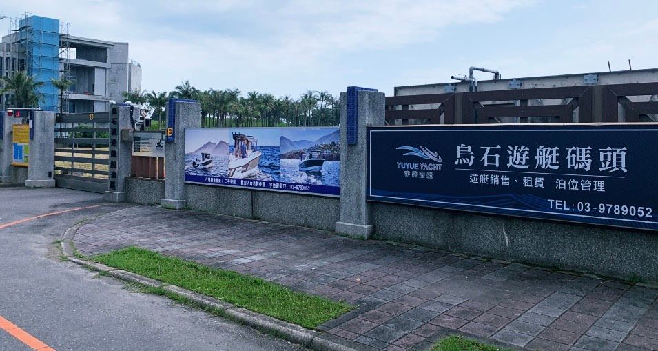 烏什遊艇港的標誌牌立在石牆上，上面掛著一幅風景優美的海岸照片和聯絡方式的橫幅。