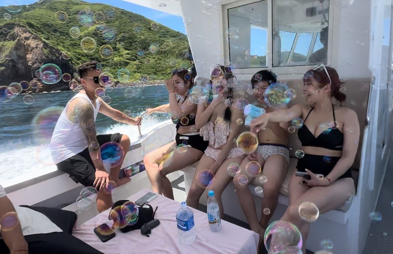 一個人在藍白相間的摩托艇的日光浴墊上放鬆休息,附近還有人在藍色的海水中游泳和漂浮。