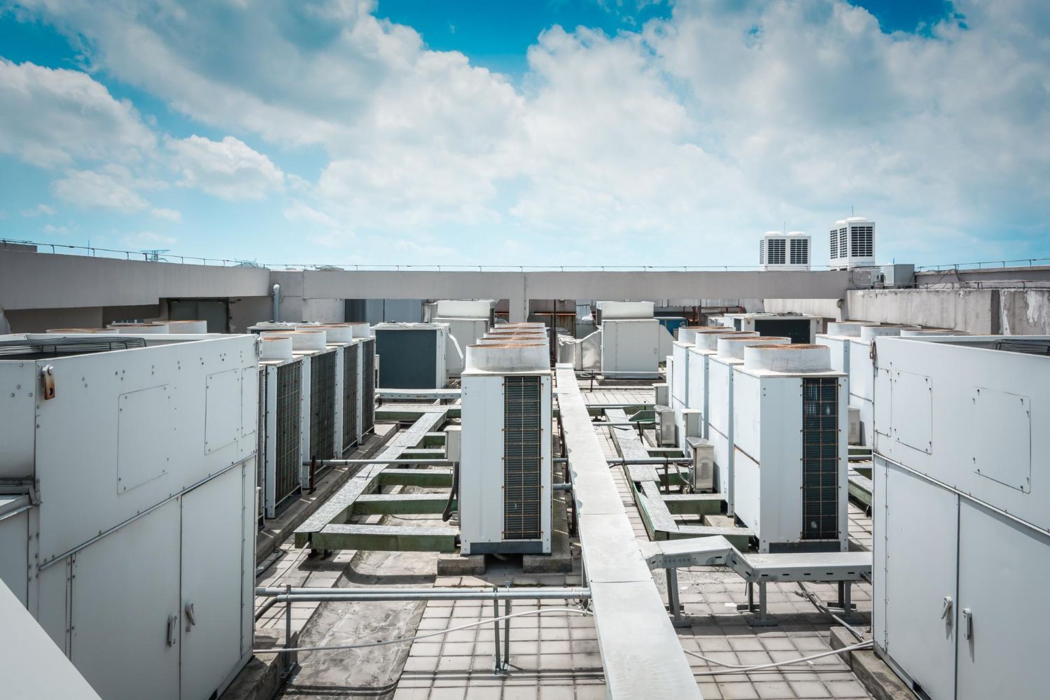 Rooftop HVAC units and piping under a blue sky with clouds