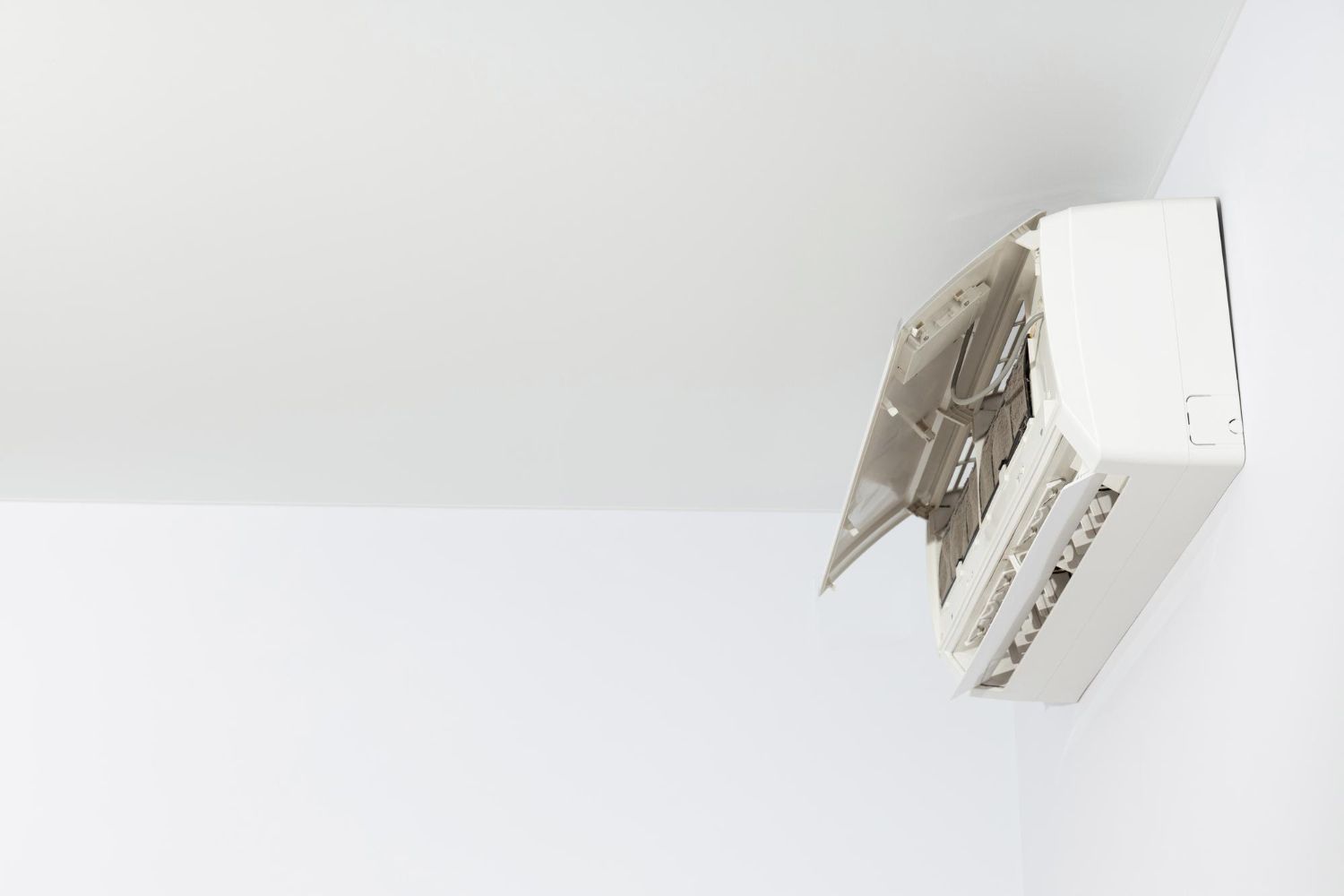 Wall-mounted air conditioner unit with open front panel on a white wall near the ceiling