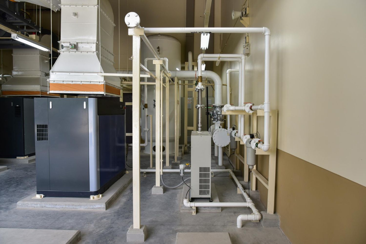 Industrial machinery and piping in a utility room with white pipes and a dark cabinet.