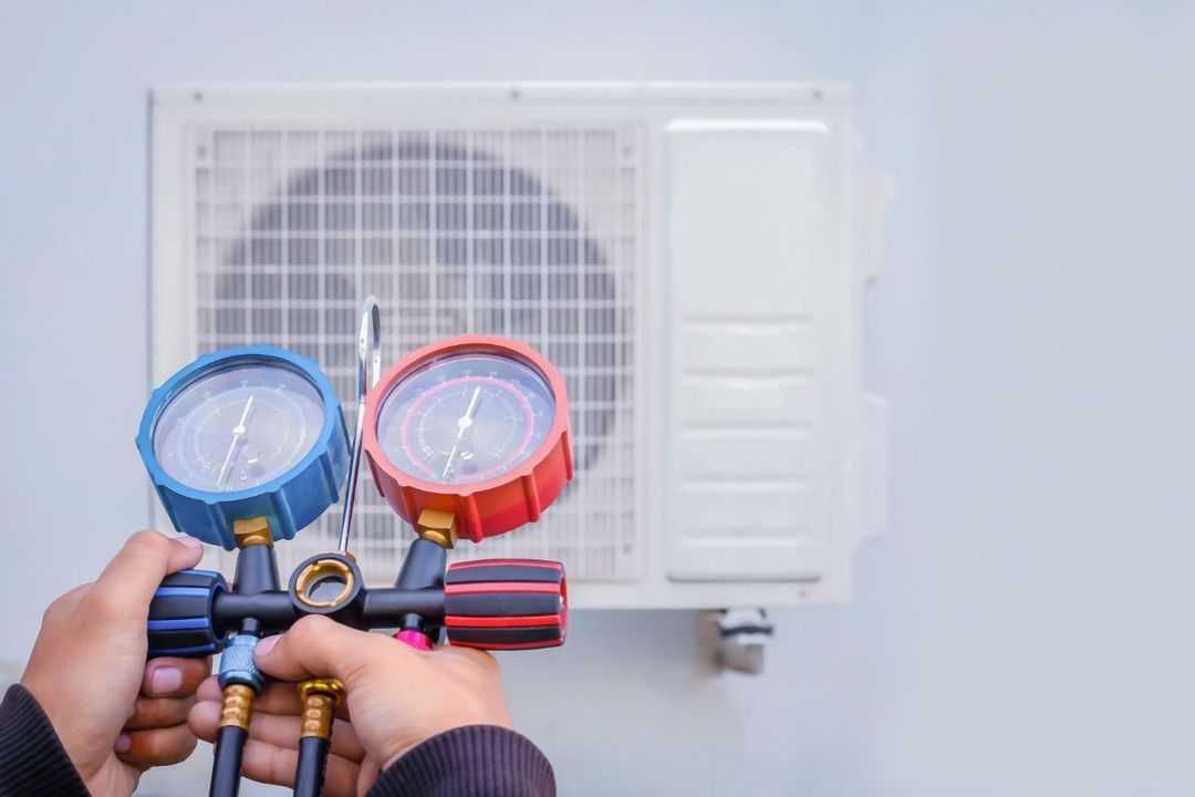 Hands holding HVAC gauges in front of an outdoor air conditioner unit