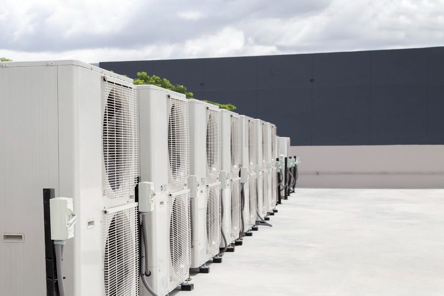 Row of white industrial HVAC units along a rooftop under a cloudy sky