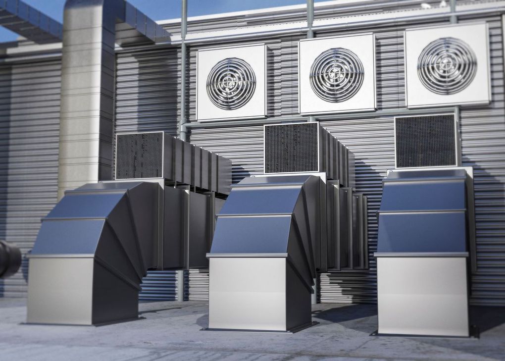 Industrial rooftop HVAC vents and ductwork beside large cooling fans on a building exterior.