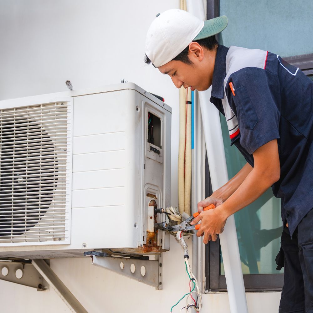 Technician in a hard hat repairing an outdoor air conditioner unit with tools