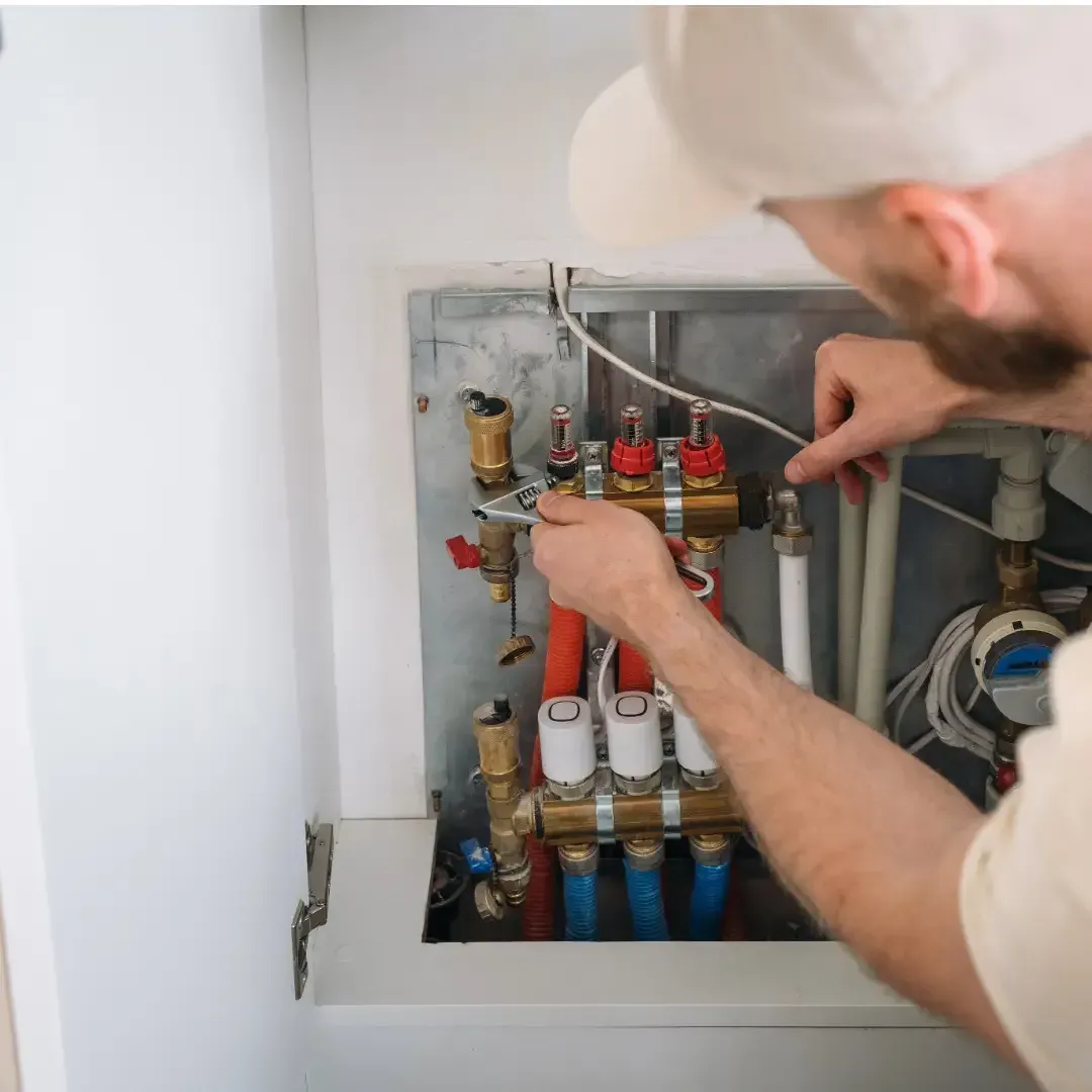 Technician adjusting valves in a utility panel with pipes and gauges