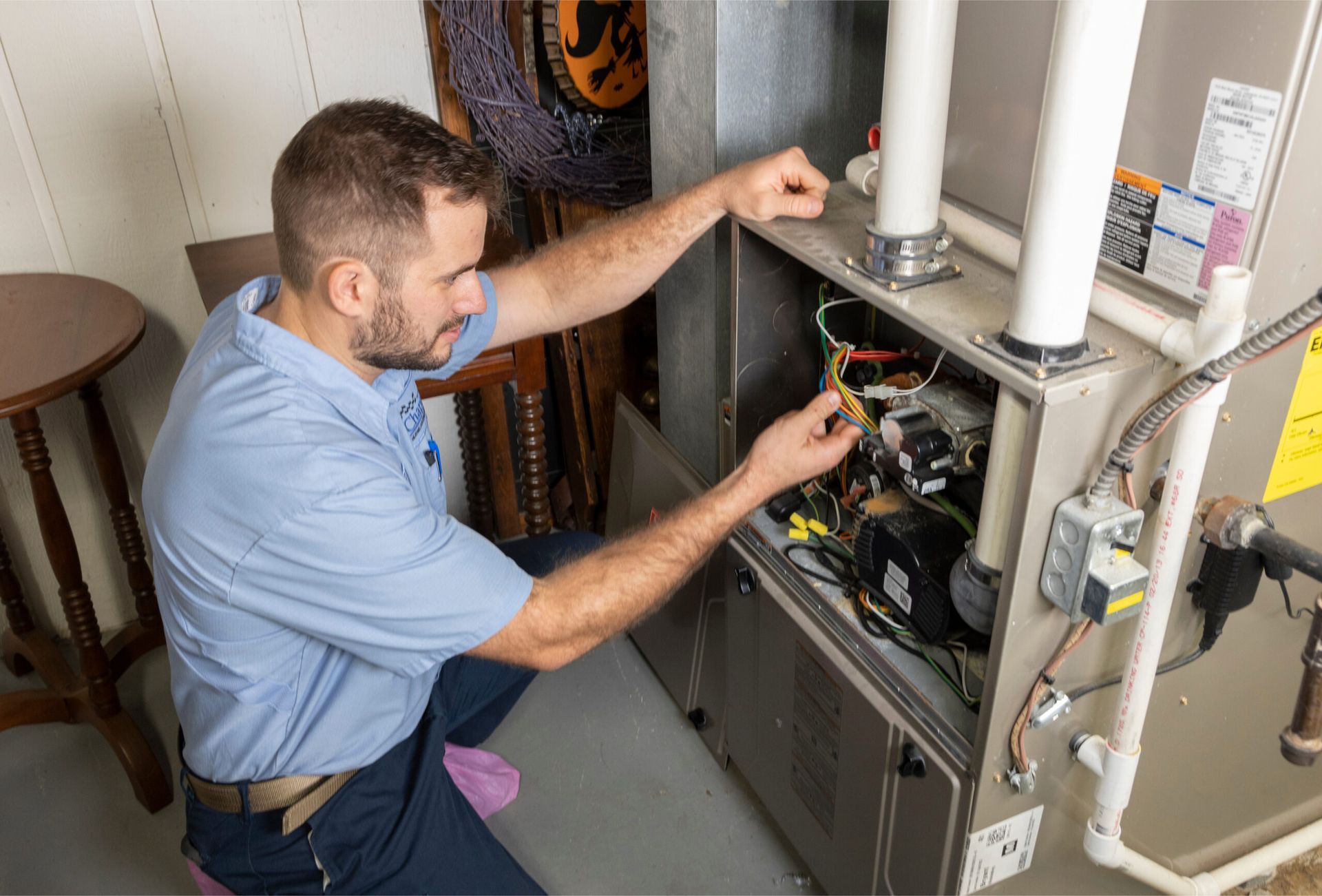 Technician inspecting wiring inside an open furnace unit in a utility room