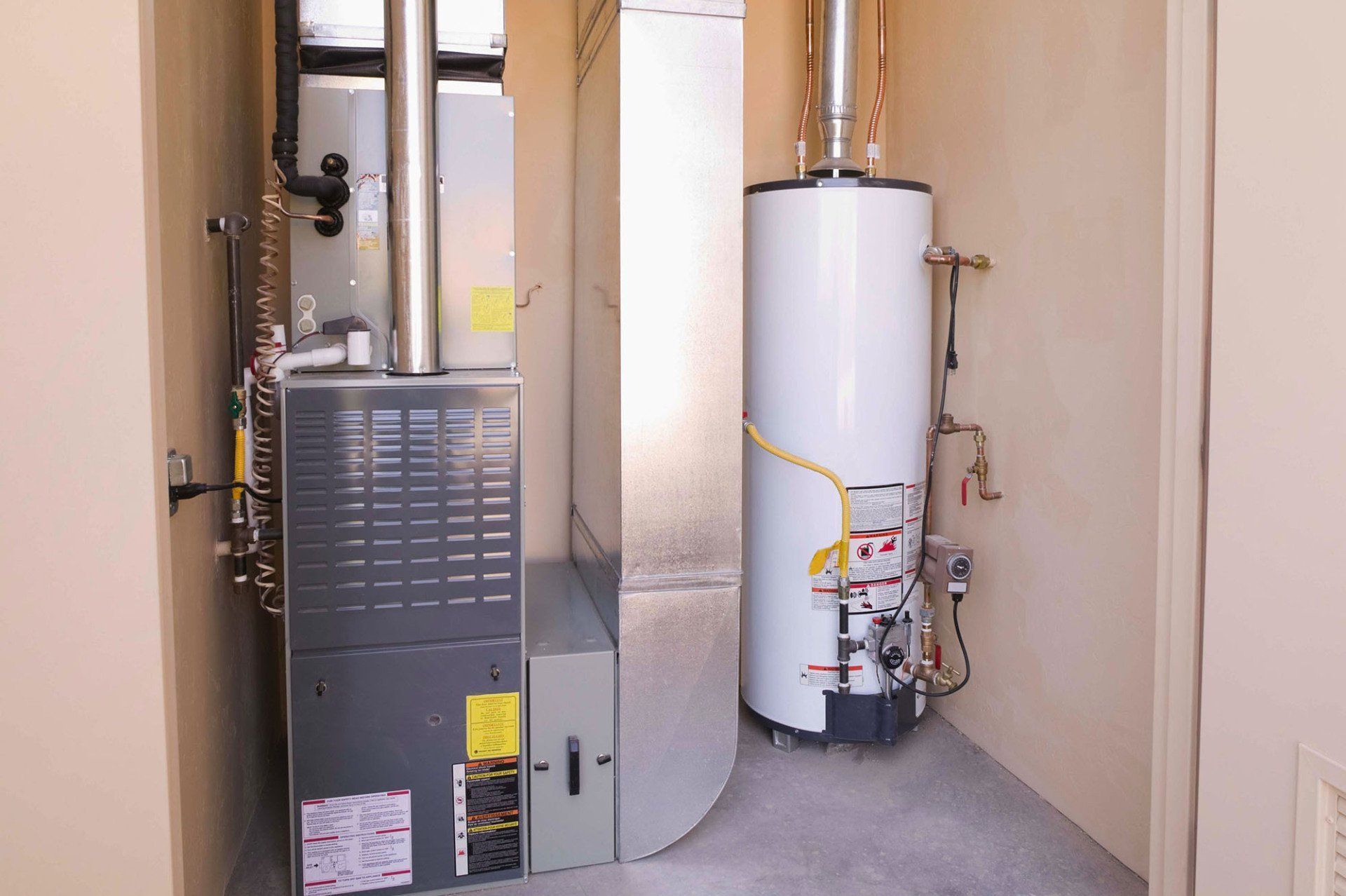 Furnace and white water heater in a narrow utility closet with exposed pipes and vents