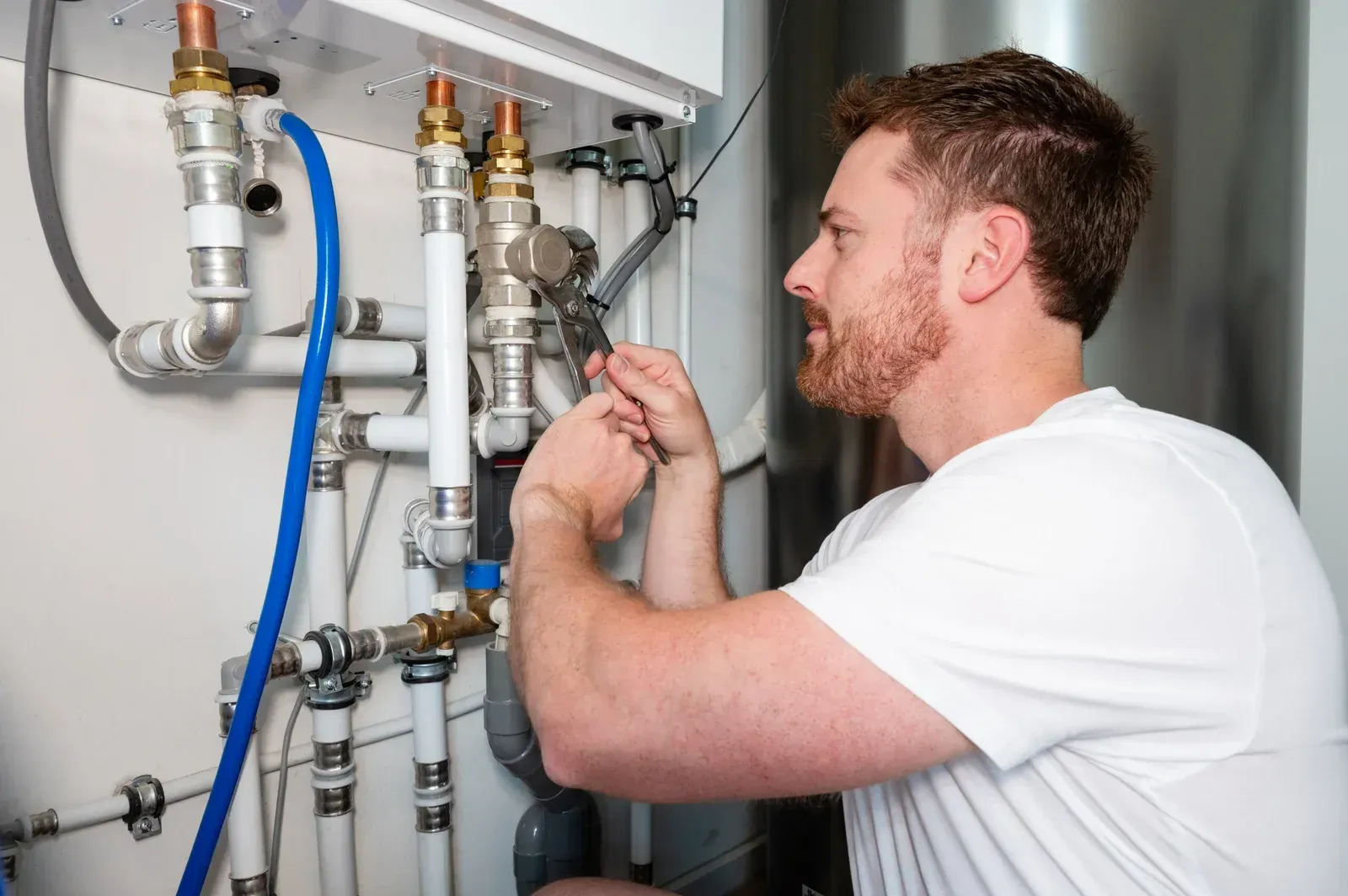 Plumber adjusting pipes and valves inside a utility cabinet with tools in hand