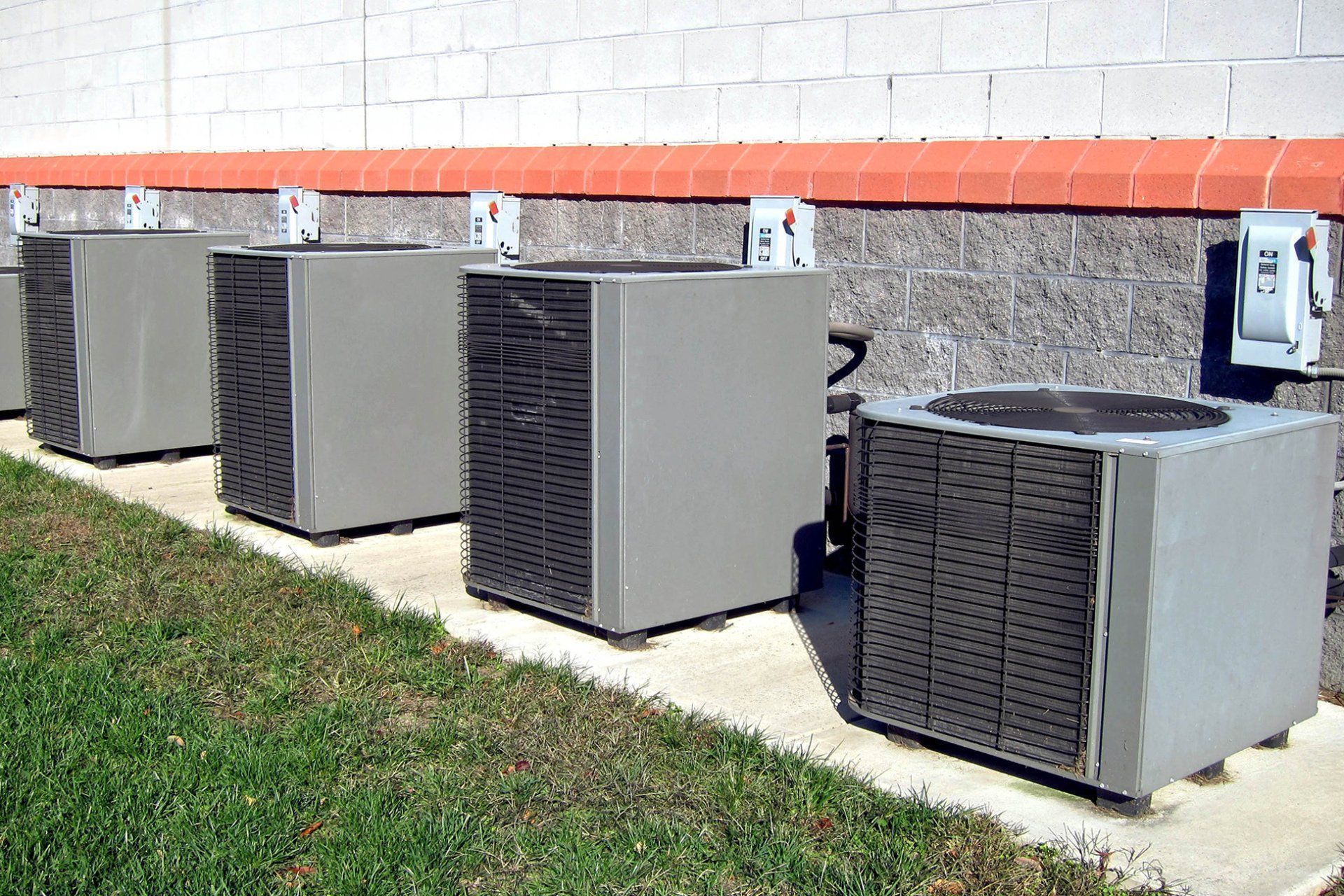 Row of outdoor air conditioning units beside a building wall on a grassy strip